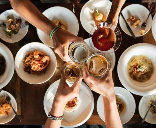 Four People Cheers Beer Glasses over Plates of Food