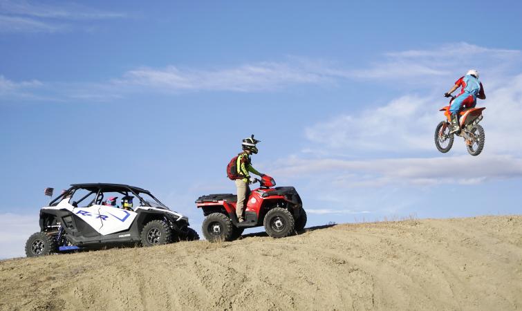 Dirtbiker jumping while people on a fourwheeler and RZR watch