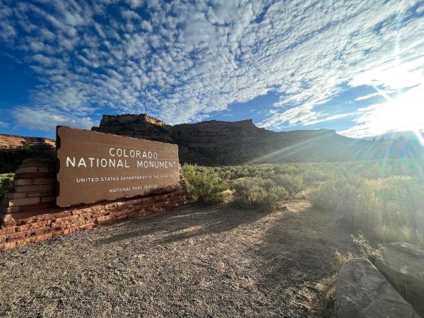 Colorado National Monument Sign Displayed in front of the Red Rocks with the Sun Shining